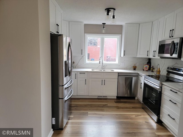 kitchen with a sink, white cabinetry, light wood-style floors, appliances with stainless steel finishes, and backsplash