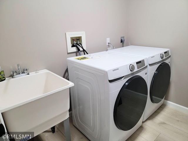 clothes washing area with laundry area, baseboards, independent washer and dryer, light wood-type flooring, and a sink