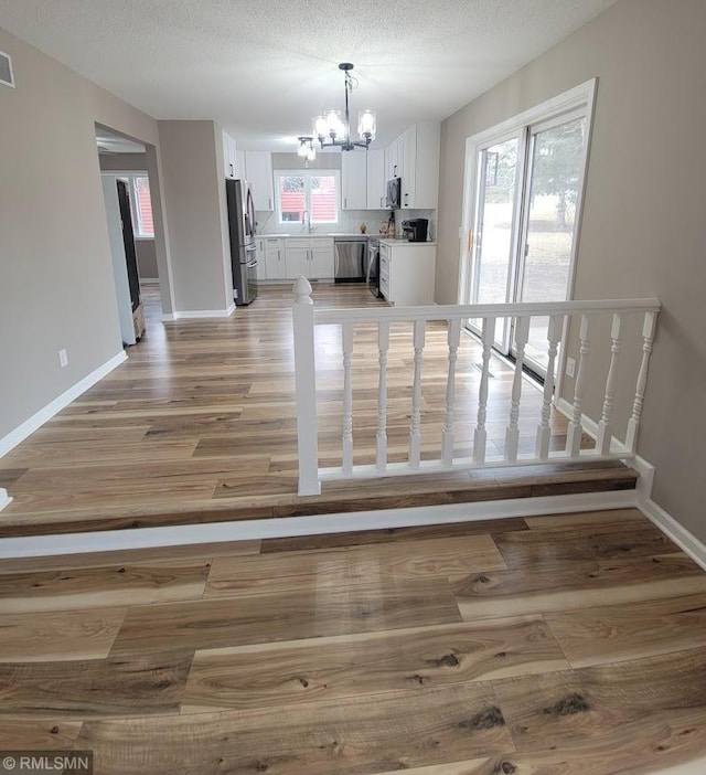 unfurnished dining area with light wood finished floors, baseboards, a textured ceiling, and an inviting chandelier