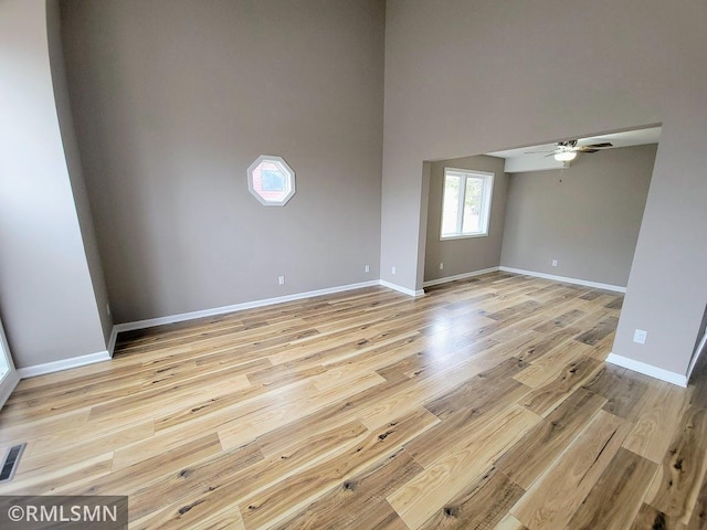 empty room featuring baseboards, visible vents, a ceiling fan, light wood-style flooring, and a high ceiling