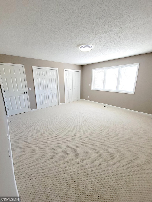 unfurnished bedroom featuring carpet, a textured ceiling, baseboards, and two closets