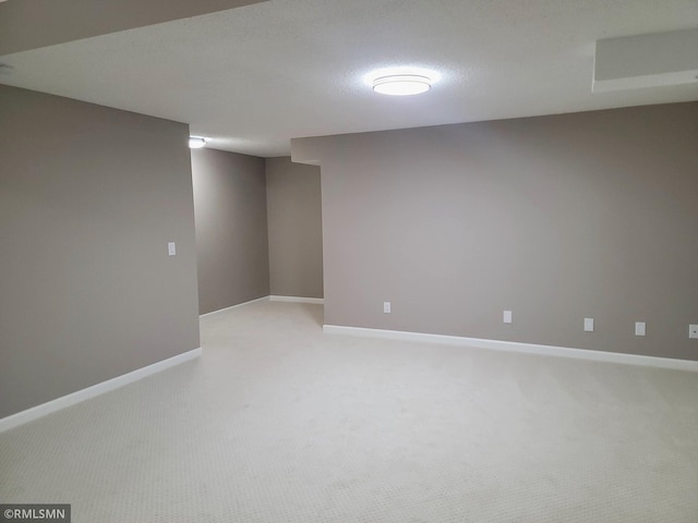 finished below grade area featuring baseboards, a textured ceiling, and light colored carpet