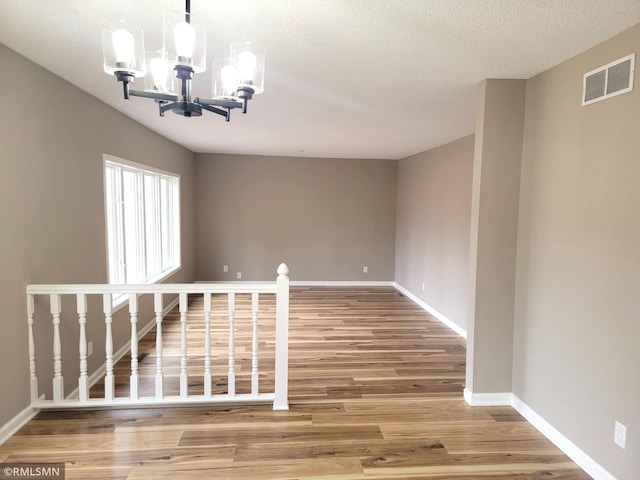 unfurnished room with a textured ceiling, a notable chandelier, wood finished floors, visible vents, and baseboards