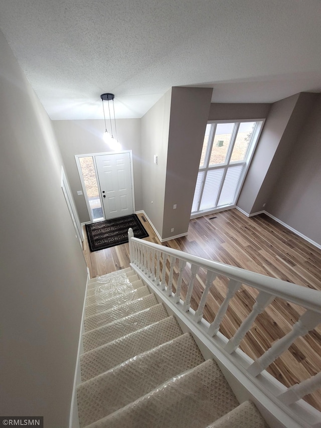 stairs featuring a textured ceiling, baseboards, and wood finished floors