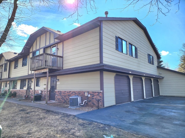 view of home's exterior featuring aphalt driveway, a balcony, central air condition unit, a garage, and brick siding