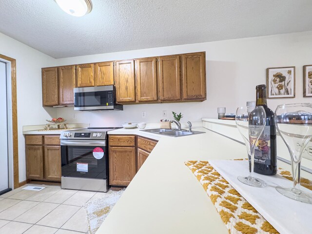 kitchen featuring appliances with stainless steel finishes, brown cabinetry, a sink, and light tile patterned floors