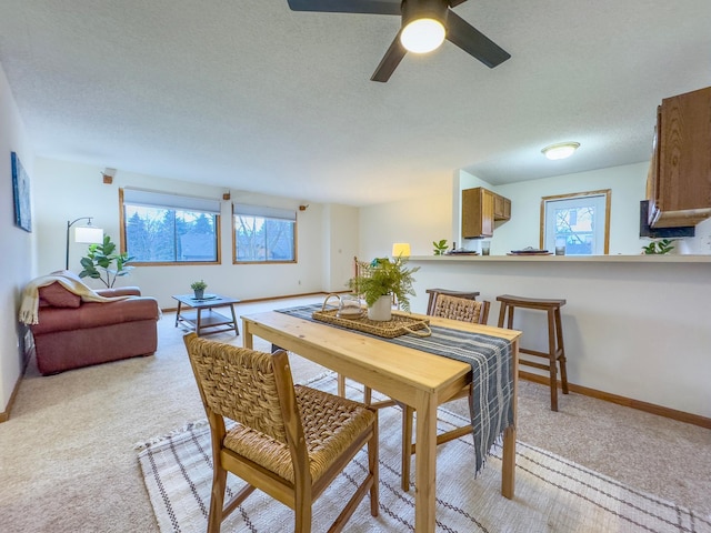 dining area with a healthy amount of sunlight, light carpet, baseboards, and a textured ceiling