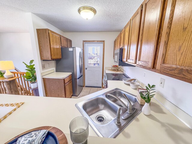 kitchen with light countertops, appliances with stainless steel finishes, a sink, and brown cabinets