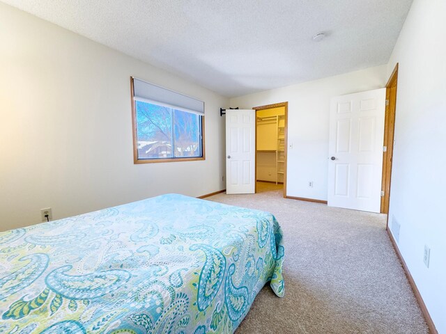 carpeted bedroom with a walk in closet, a textured ceiling, and baseboards