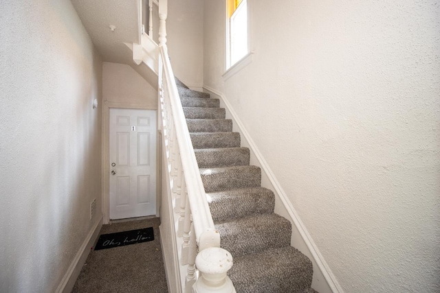 staircase featuring a textured wall and carpet flooring