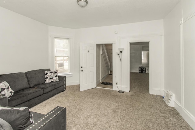 living area with baseboards, visible vents, and light colored carpet