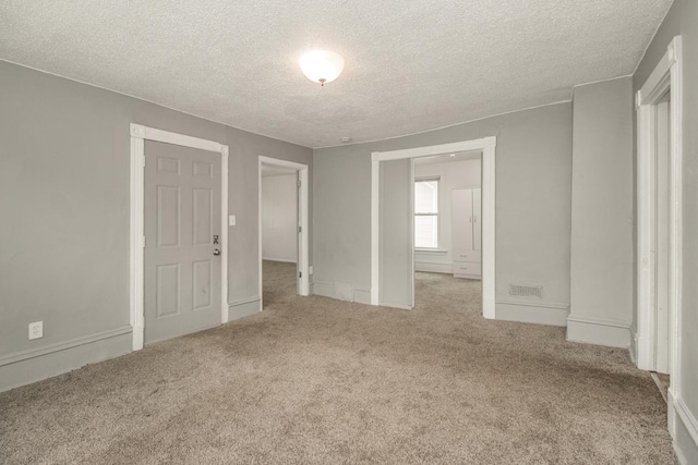 unfurnished room with light colored carpet, visible vents, and a textured ceiling