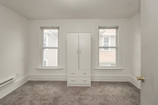 unfurnished bedroom with baseboards, a baseboard heating unit, a textured ceiling, and light colored carpet