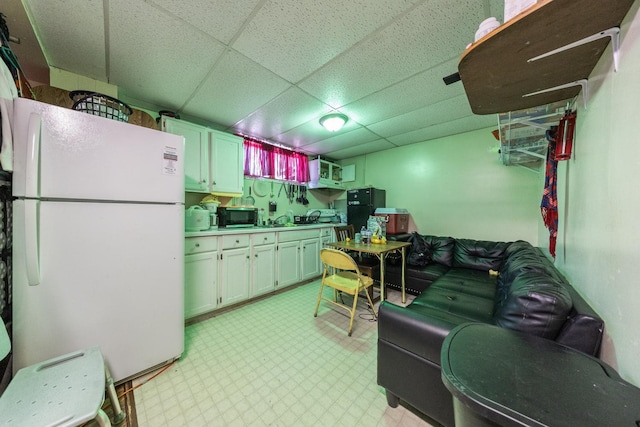 kitchen with a drop ceiling, a sink, light countertops, freestanding refrigerator, and light floors