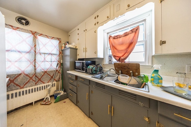 kitchen with radiator, stainless steel microwave, light countertops, and a sink