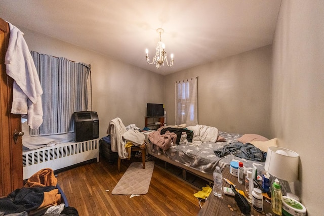 bedroom featuring wood finished floors, radiator heating unit, and an inviting chandelier