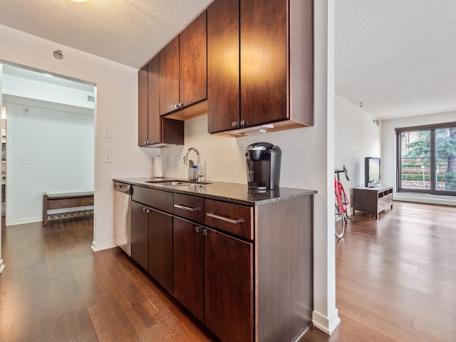 kitchen with dark wood finished floors, dark stone countertops, a sink, a textured ceiling, and stainless steel dishwasher