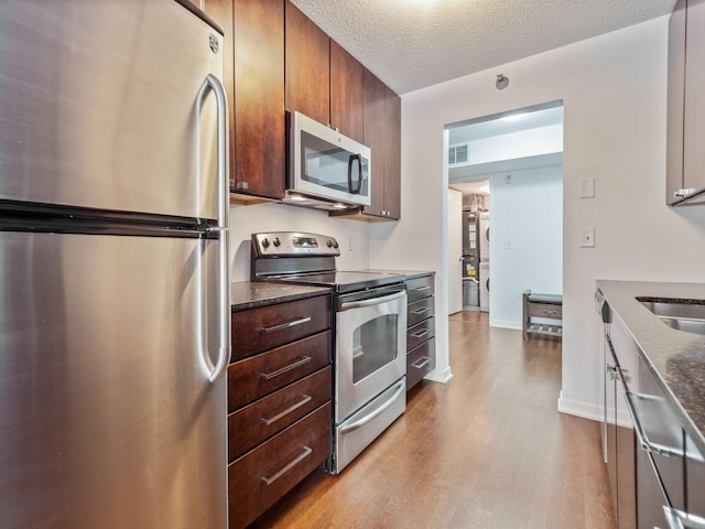 kitchen featuring a textured ceiling, stainless steel appliances, visible vents, light wood-style floors, and dark stone countertops