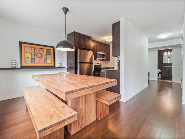 kitchen featuring baseboards, dark brown cabinets, appliances with stainless steel finishes, dark wood finished floors, and decorative light fixtures