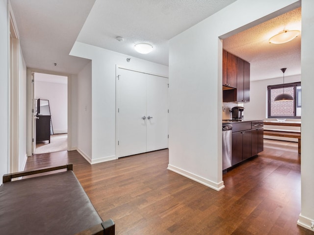 corridor featuring a textured ceiling, dark wood-type flooring, and baseboards