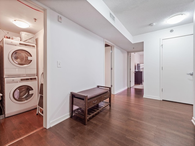 laundry room with a textured ceiling, dark wood-type flooring, visible vents, baseboards, and stacked washer / drying machine