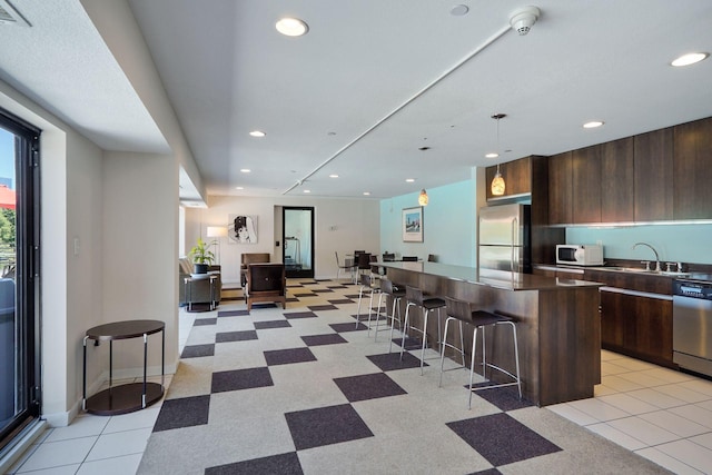 kitchen with a center island, a breakfast bar, dark countertops, appliances with stainless steel finishes, and a sink