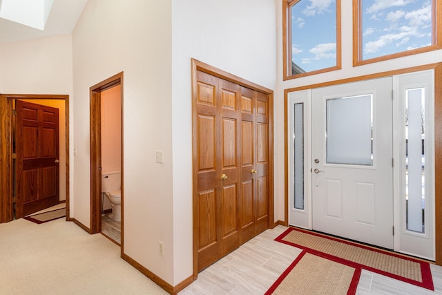 foyer entrance with a skylight, a towering ceiling, and baseboards