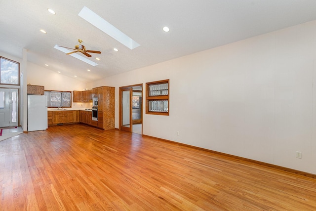 unfurnished living room featuring a skylight, light wood finished floors, a ceiling fan, high vaulted ceiling, and a sink