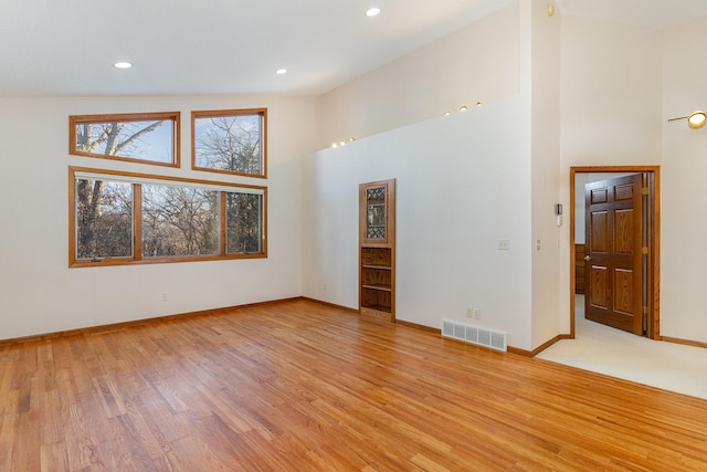 unfurnished room with recessed lighting, visible vents, a high ceiling, light wood-type flooring, and baseboards