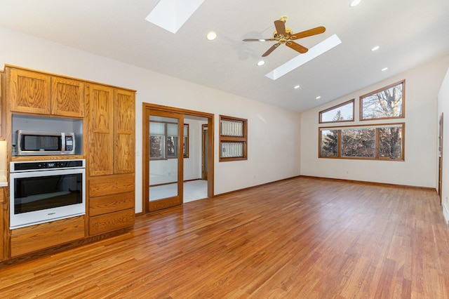 kitchen featuring wall oven, a skylight, stainless steel microwave, brown cabinets, and light wood-style floors