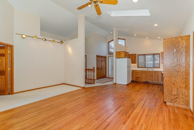 unfurnished living room featuring a skylight, light wood finished floors, a textured ceiling, high vaulted ceiling, and baseboards