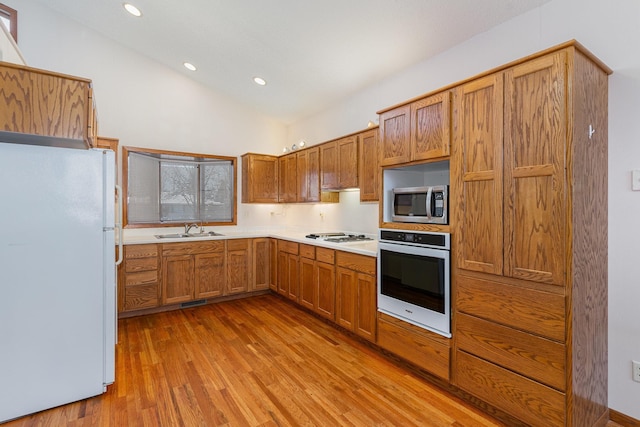 kitchen featuring light wood-style flooring, white appliances, a sink, vaulted ceiling, and light countertops