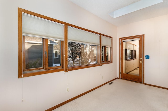 spare room featuring light carpet, a skylight, baseboards, and visible vents