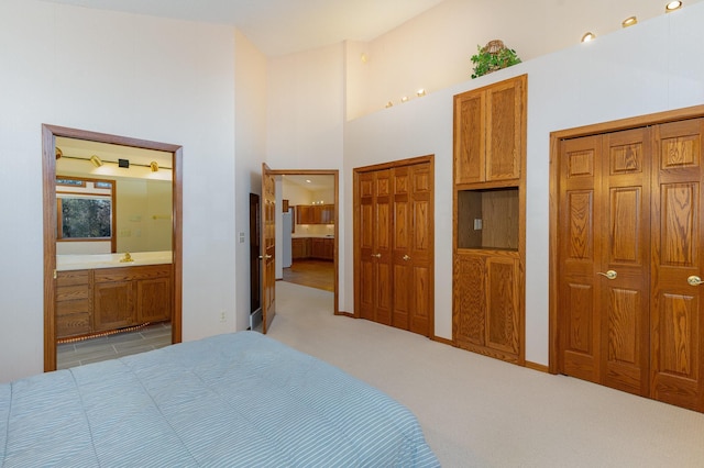 bedroom with a towering ceiling, connected bathroom, two closets, and light colored carpet