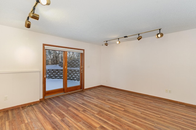 unfurnished room with a textured ceiling, wood finished floors, visible vents, and baseboards