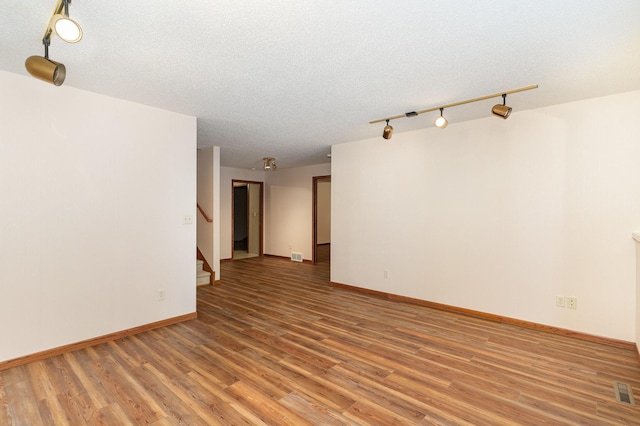 unfurnished room featuring visible vents, a textured ceiling, wood finished floors, baseboards, and stairs