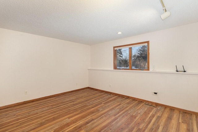 empty room featuring a textured ceiling, wood finished floors, visible vents, and baseboards