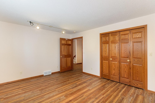 unfurnished bedroom featuring light wood finished floors, baseboards, visible vents, a textured ceiling, and a closet