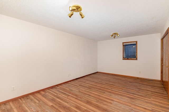 spare room with light wood-style floors, baseboards, and a textured ceiling