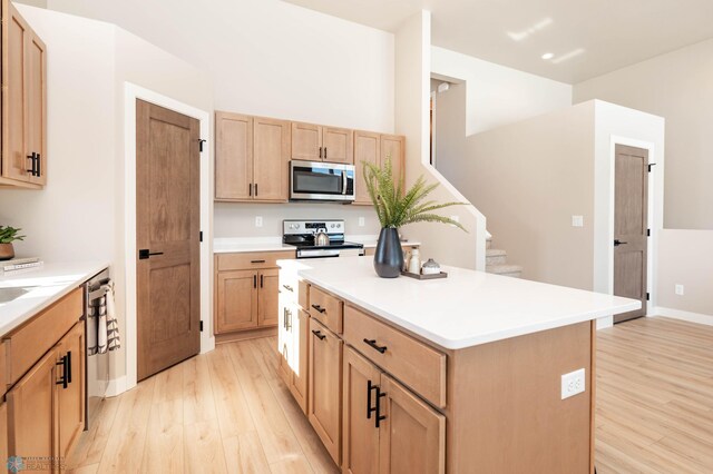 kitchen with light countertops, appliances with stainless steel finishes, a center island, and light wood finished floors