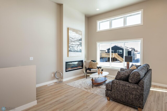 sitting room with a glass covered fireplace, a high ceiling, baseboards, and wood finished floors