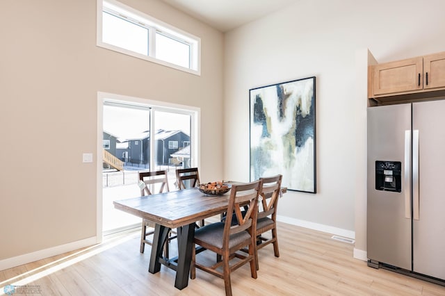 dining space with visible vents, baseboards, a high ceiling, and light wood-style floors