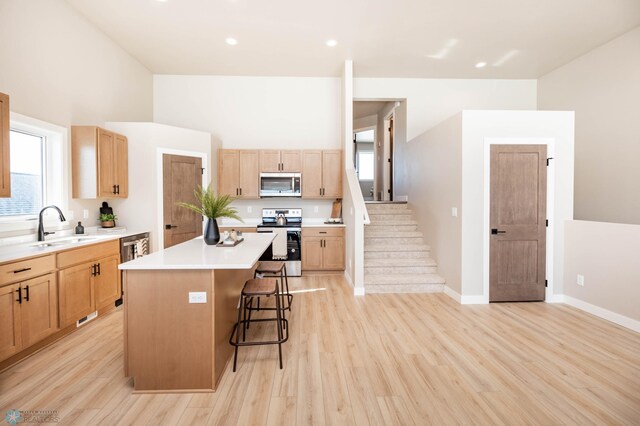 kitchen featuring light wood-style flooring, a sink, a center island, stainless steel appliances, and a breakfast bar area