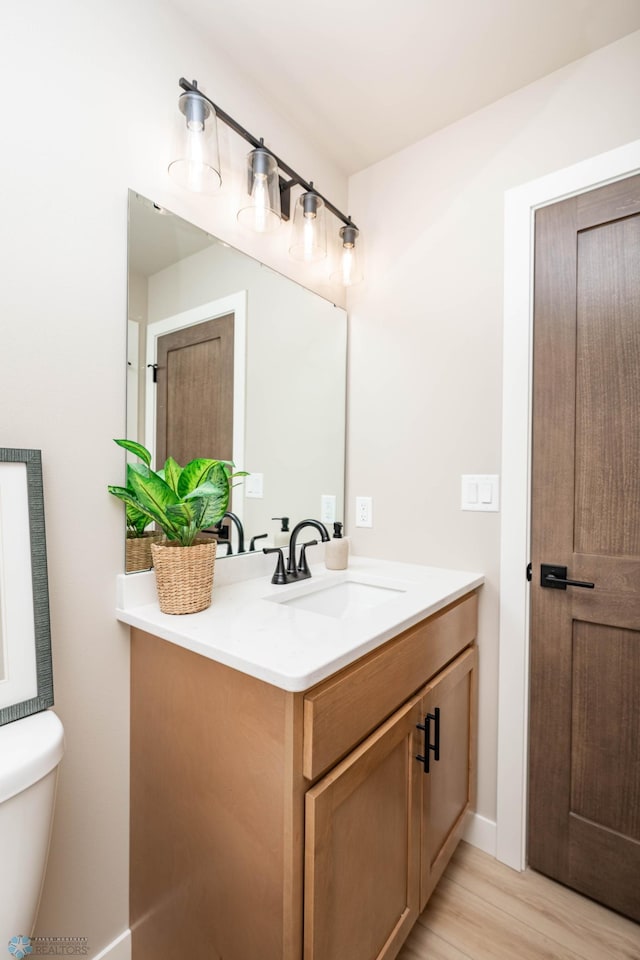 half bath with toilet, wood finished floors, and vanity