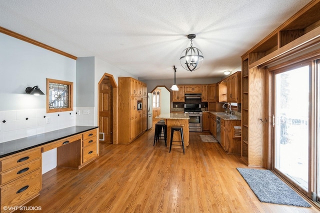 kitchen featuring a sink, a kitchen breakfast bar, appliances with stainless steel finishes, open shelves, and brown cabinetry