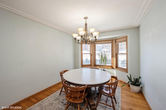 dining area with light wood-style flooring, a textured ceiling, a chandelier, and baseboards