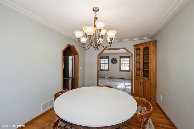 dining space with arched walkways, light wood-style flooring, visible vents, and an inviting chandelier