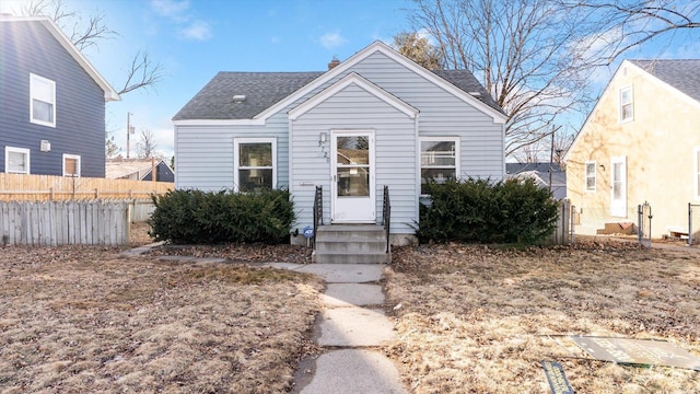 bungalow-style home with a shingled roof, entry steps, fence, and a chimney