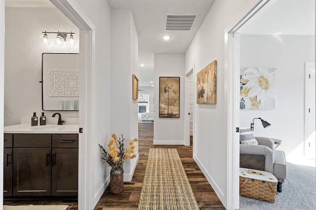 corridor featuring baseboards, visible vents, dark wood-type flooring, and a sink