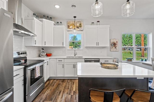 kitchen with stainless steel appliances, a sink, white cabinetry, light countertops, and decorative light fixtures